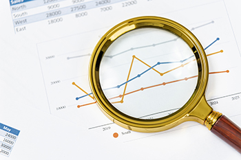 Insights drawn from data analysis using a magnifying glass on gr A magnifying glass rests over printed graphs showing data trends for various regions. The lines fluctuate, revealing insights for future forecasts and analysis.