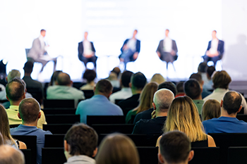 Rear view of the audience at a business conference meeting event listening to the speakers speech Rear view of the audience at a business conference meeting event listening to the speakers speech