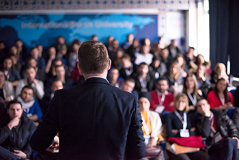 successful businessman giving presentations at conference room rear view of young successful businessman at business conference room with public giving presentations. Audience at the conference hall. Entrepreneurship club