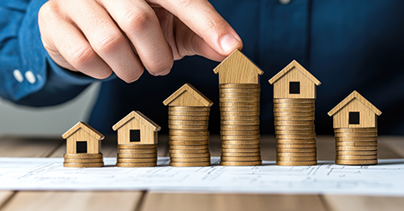 Household debt planning concept. A hand stacking a house model o Person highlighting a financial plan with a house blueprint on the table